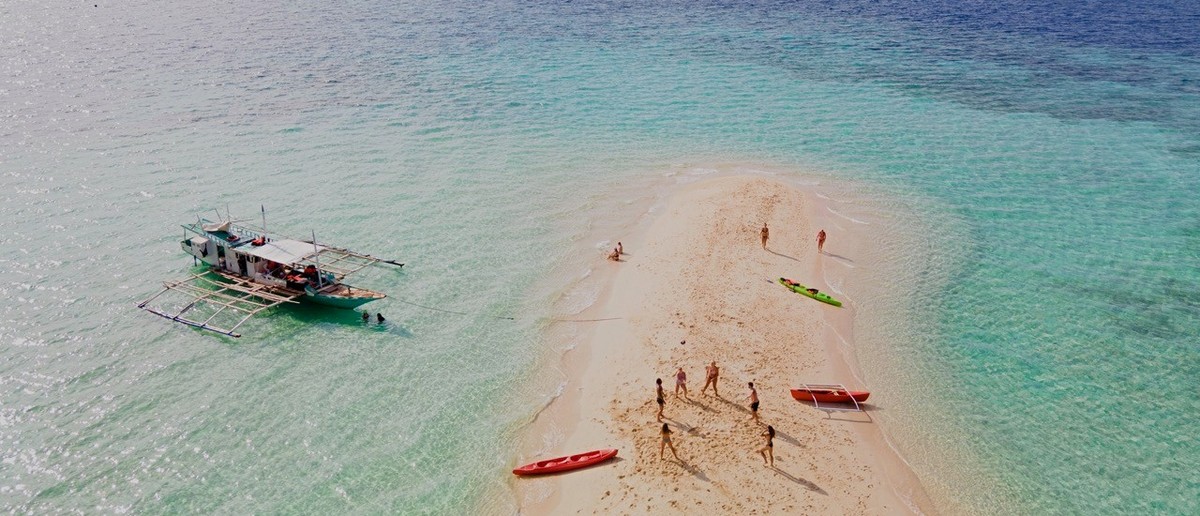 An aerial view of a white sand bar in the middle of turquoise water in Palawan.