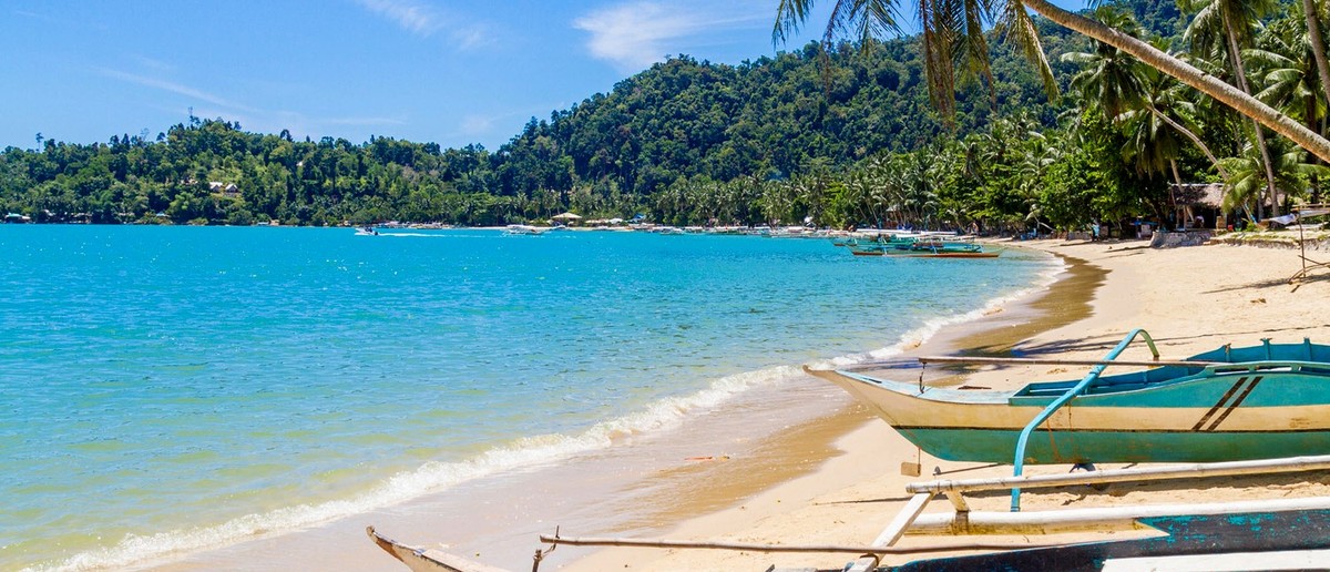 A boat crossing turquoise water between tropical islands in Palawan.