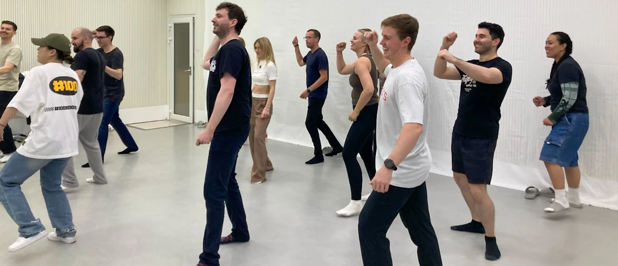 A diverse group of young adults enthusiastically learning K-pop dance moves in a bright studio in Seoul.