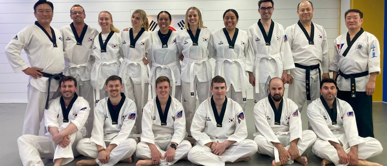 A group of happy students and instructors in white taekwondo uniforms pose for a photo in Gyeongju.