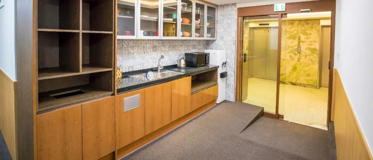 A clean hostel kitchenette with wooden cabinets, a sink, and an elevator entrance in Seoul.