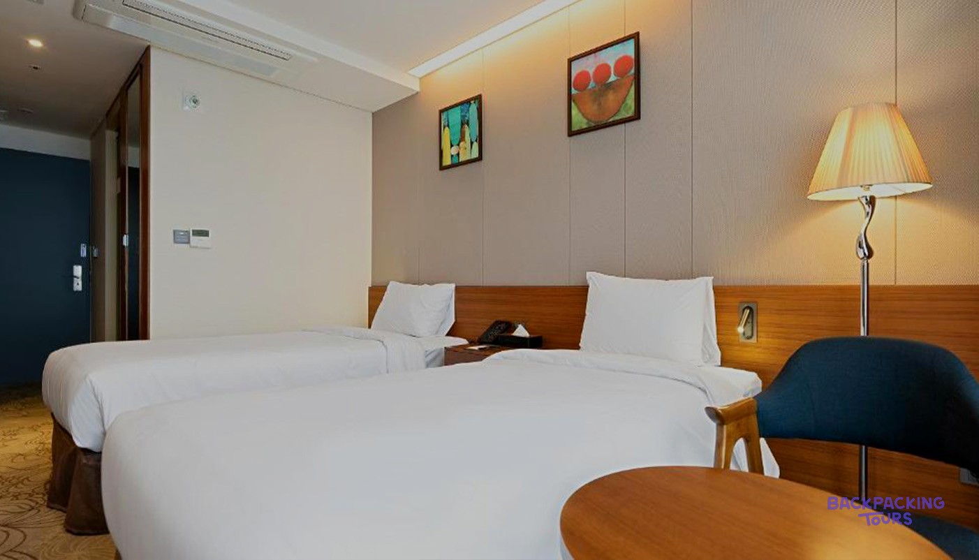 A bright twin room at the Gloucester Hotel Jeonju with two beds and a reading lamp.