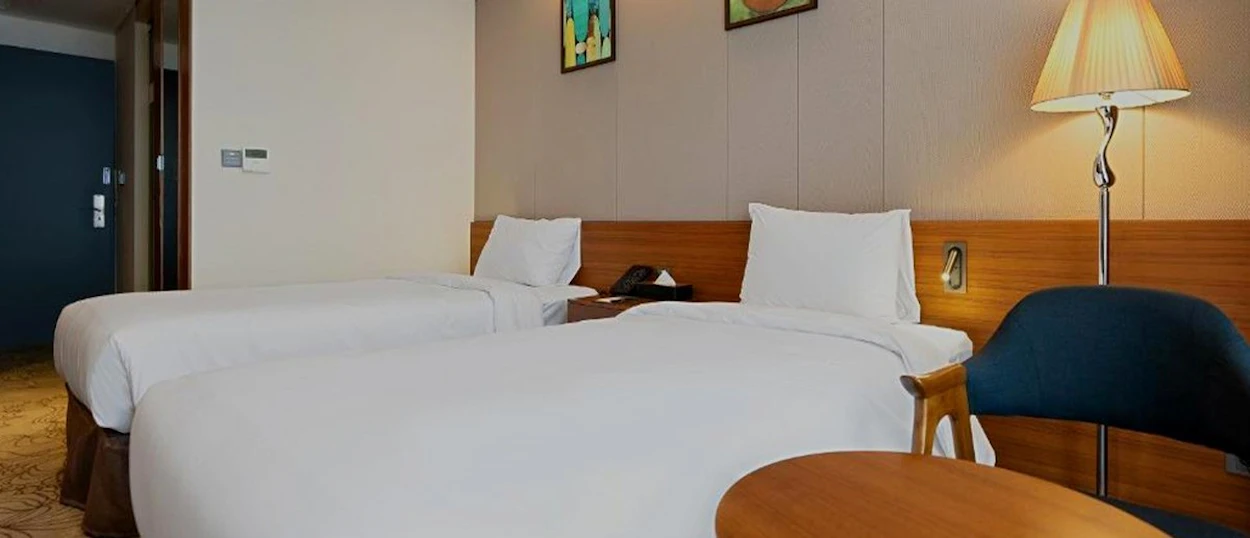 A bright twin room at the Gloucester Hotel Jeonju with two beds and a reading lamp.