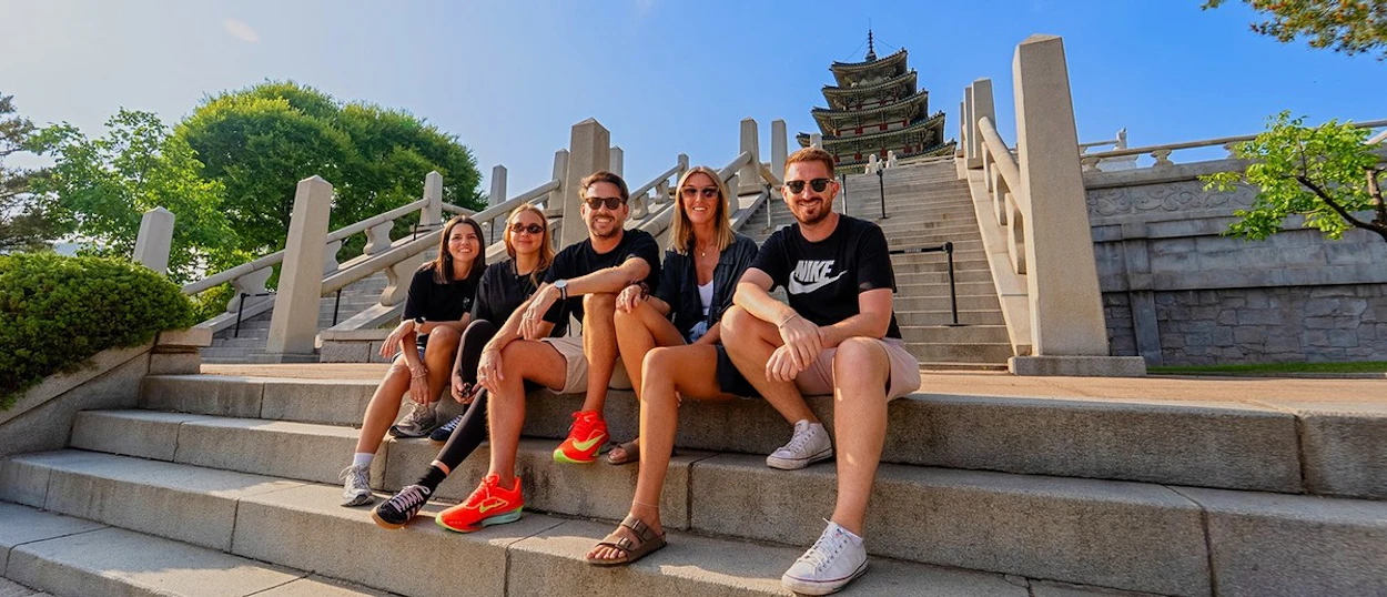 A group of travellers sitting on the stone steps in front of Gyeongbokgung Palace in Seoul.