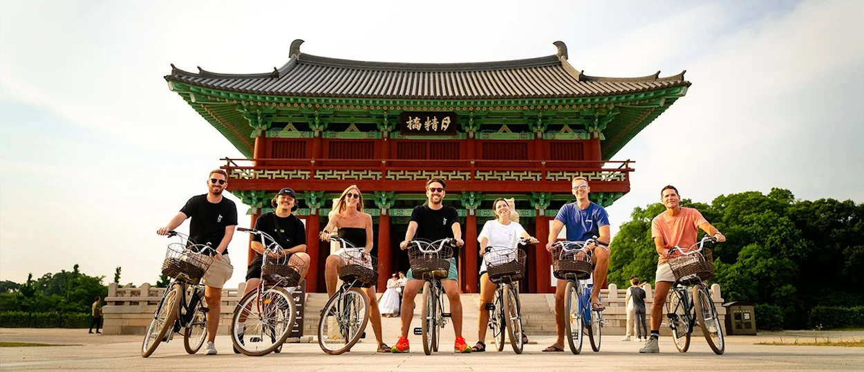 A group of cyclists lined up with their bikes in front of a traditional gate in Gyeongju.