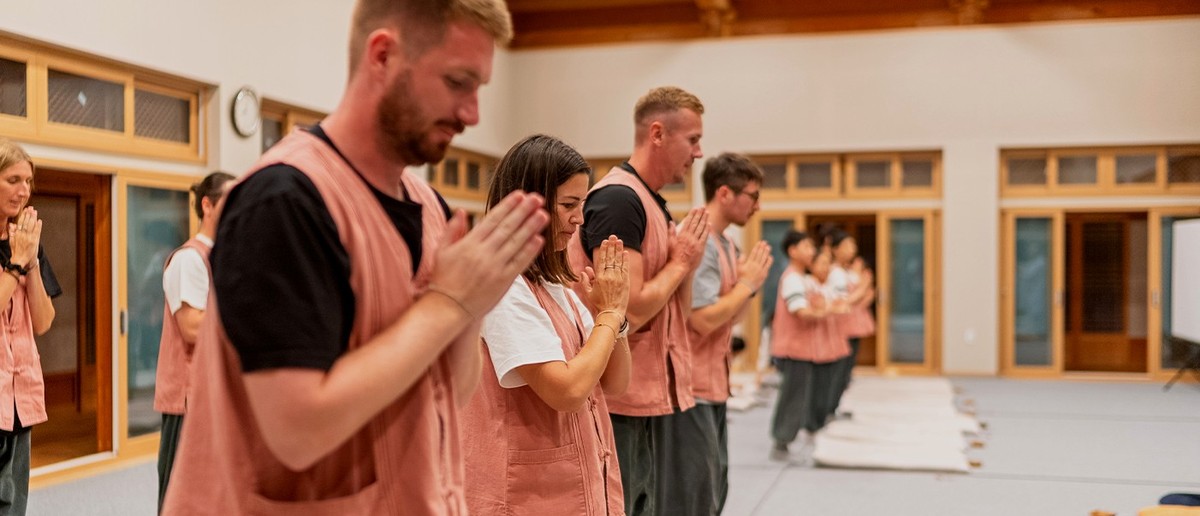 Travellers in temple-stay vests standing with hands pressed together during prayers at a Buddhist temple.