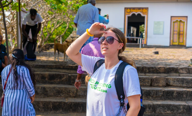 A young woman wearing sunglasses shields her eyes from the sun at the Dambulla Cave Temple.