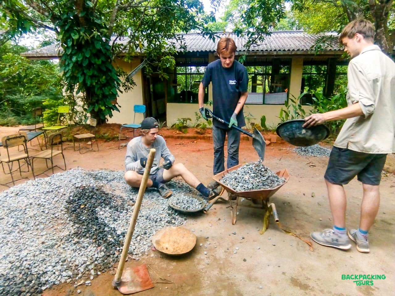 Volunteers work together, shoveling gravel for a renovation project in the lush Sri Lankan countryside.