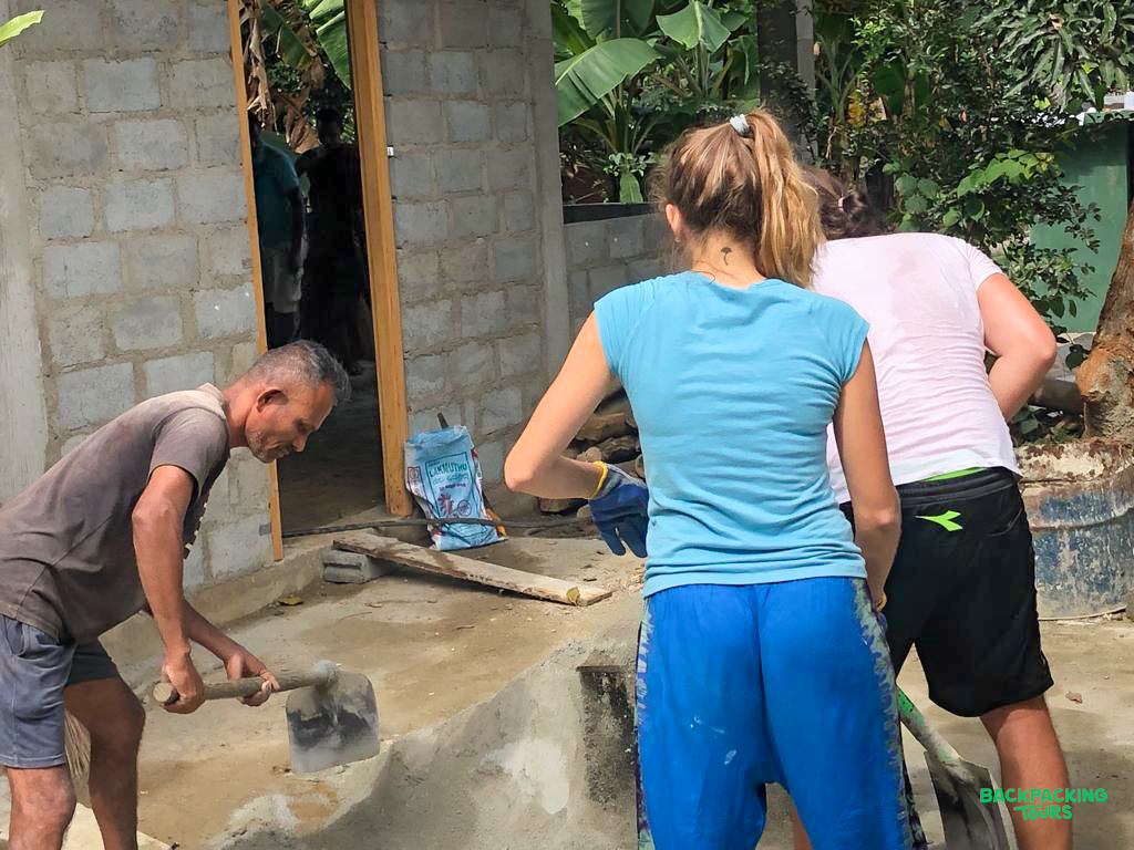 Volunteers and local workers construct a building in the lush Sri Lankan countryside.