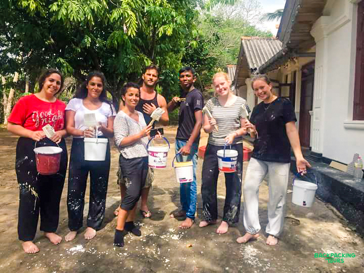 Smiling volunteers with paint-splattered clothes and tools pose proudly after renovation work in Sri Lanka.