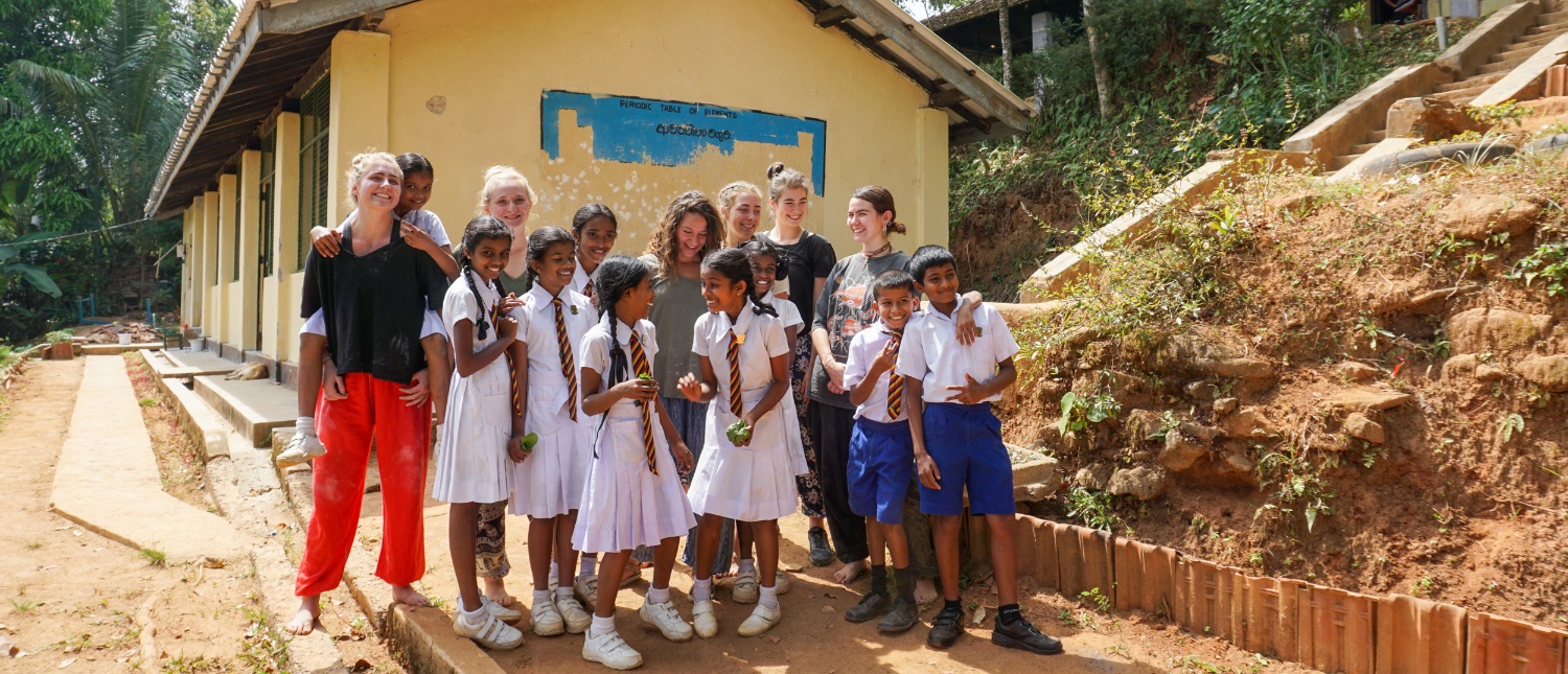 Happy volunteers and local students pose together outside a school building in Sri Lanka.