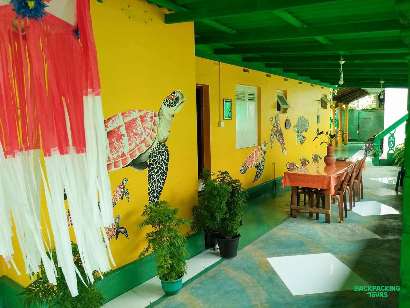 Colorful Sri Lankan guesthouse with bright yellow walls, green trim, and charming sea turtle murals.