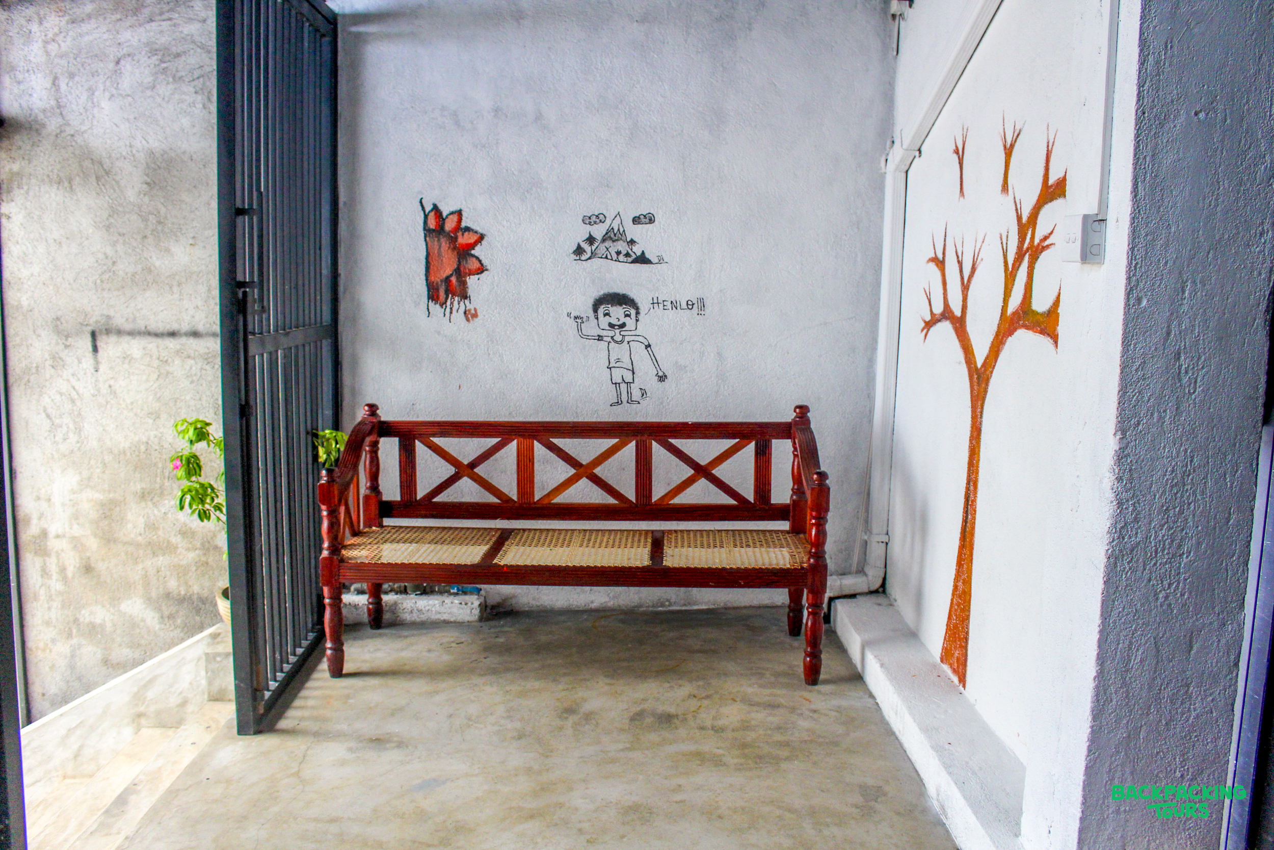 The welcoming front gate of a Sri Lankan accommodation with a wooden bench and colorful wall art.