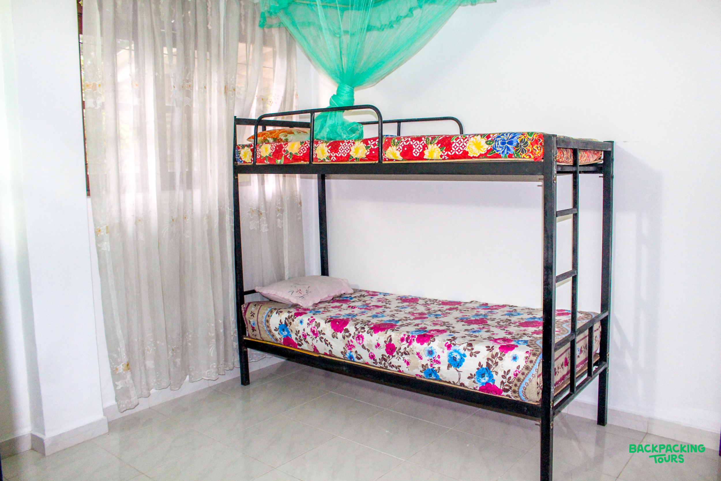 A simple bunk bed with colorful mattresses and a green mosquito net in Sri Lankan accommodation.