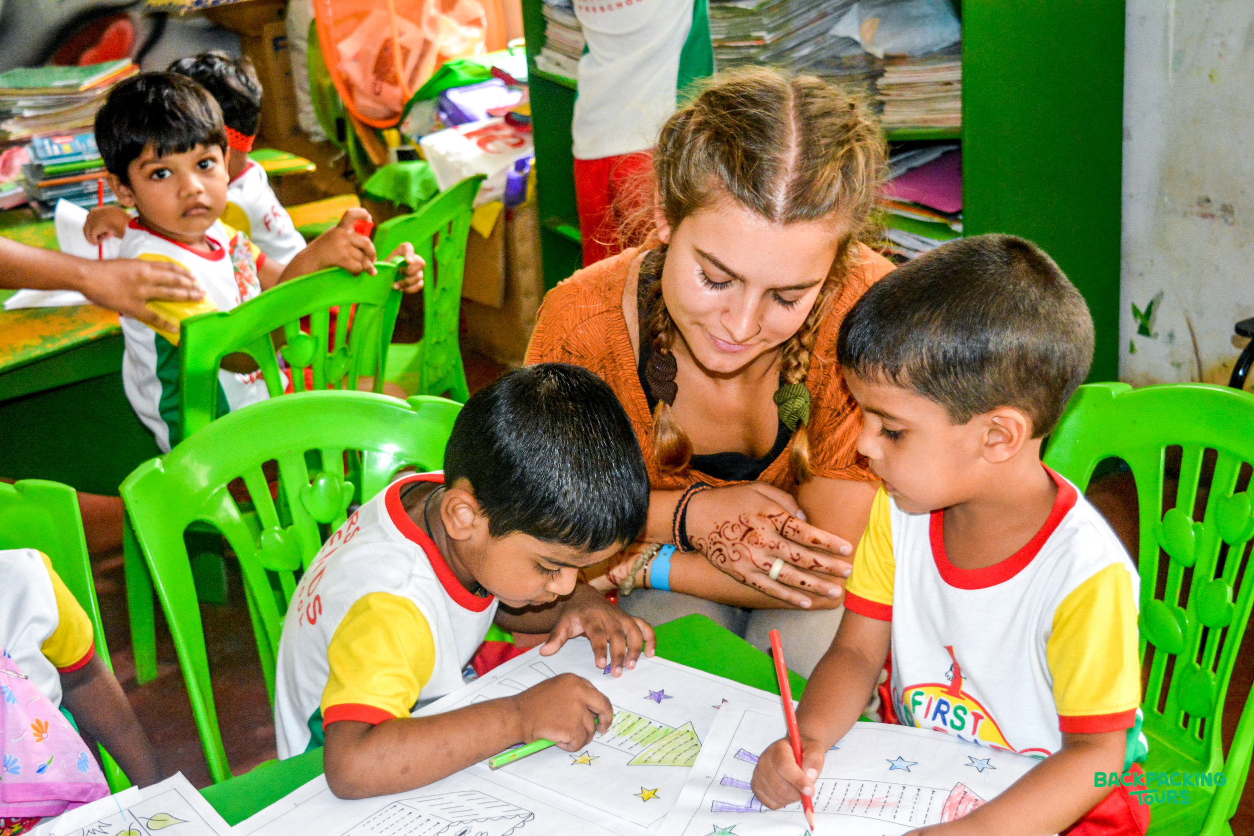 A volunteer helps young children with their coloring activity in a bright classroom in Sri Lanka.
