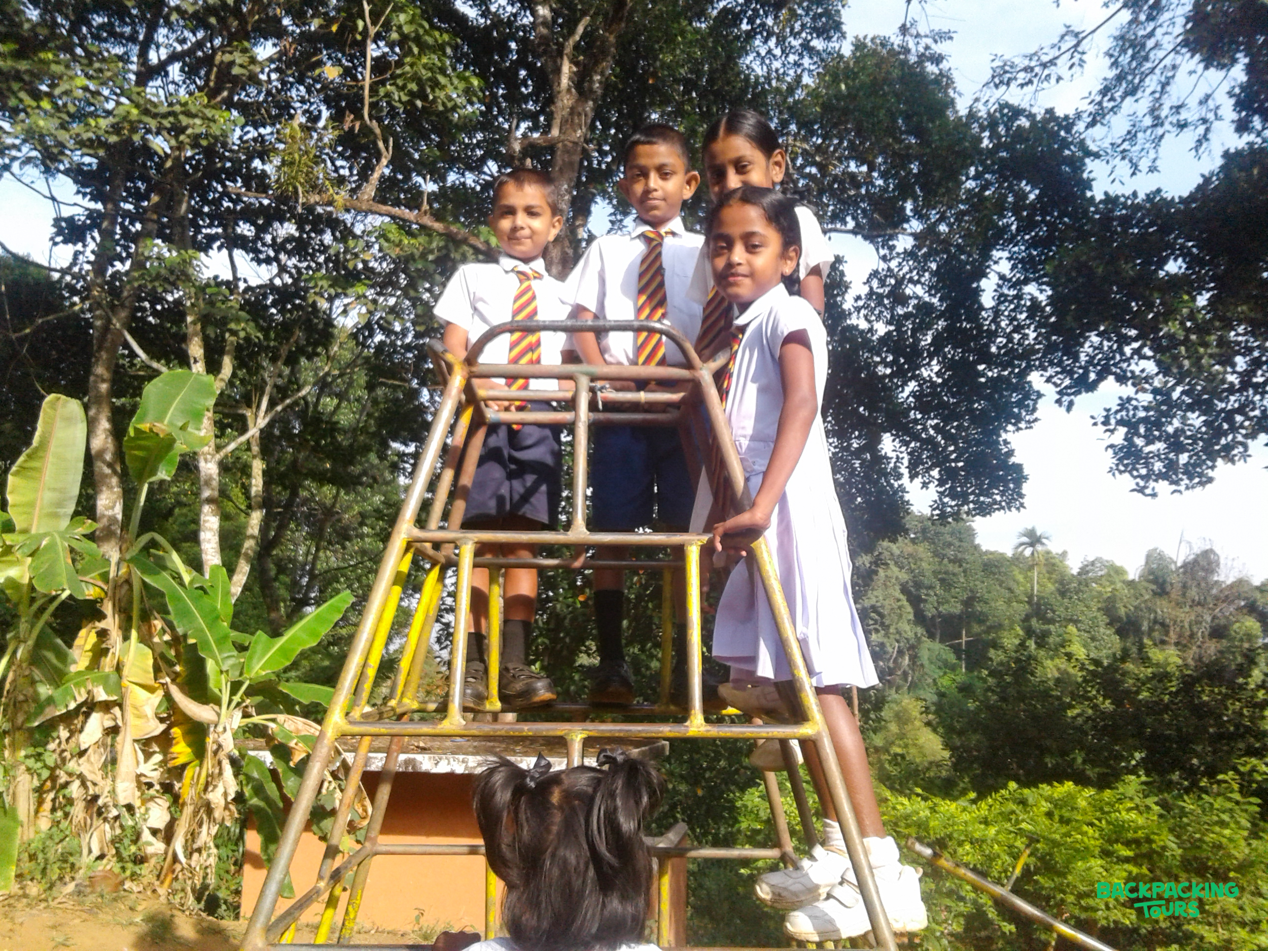 Cheerful Sri Lankan children in school uniforms playing on a metal structure in the lush countryside.