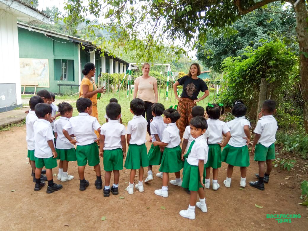Volunteers interact with a group of young students in uniforms at a school in Sri Lanka.