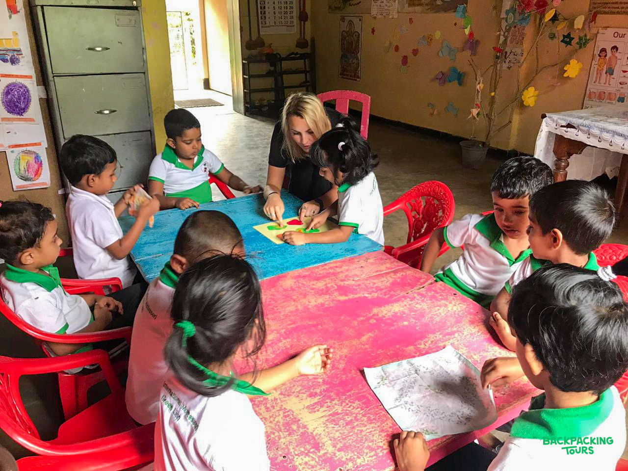 A volunteer teacher guides young Sri Lankan children in a colorful classroom activity.