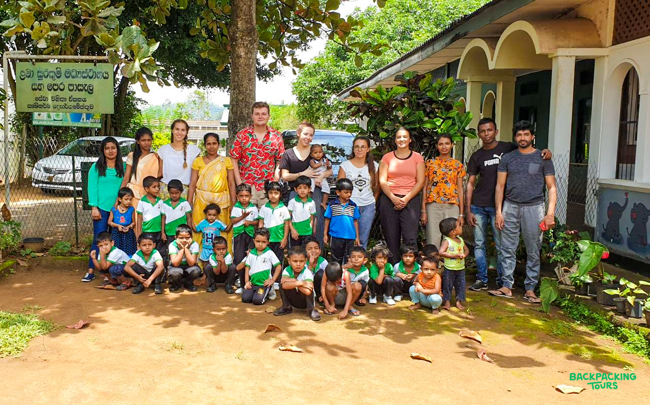 Volunteer teachers and local children pose happily together in the lush Sri Lankan countryside.