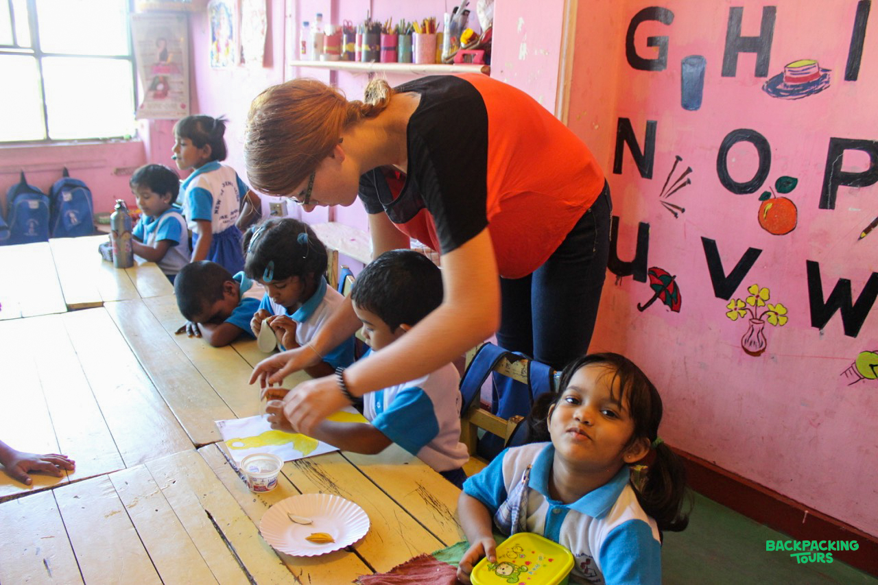 A volunteer teacher guides young students during a creative activity in a colorful classroom.