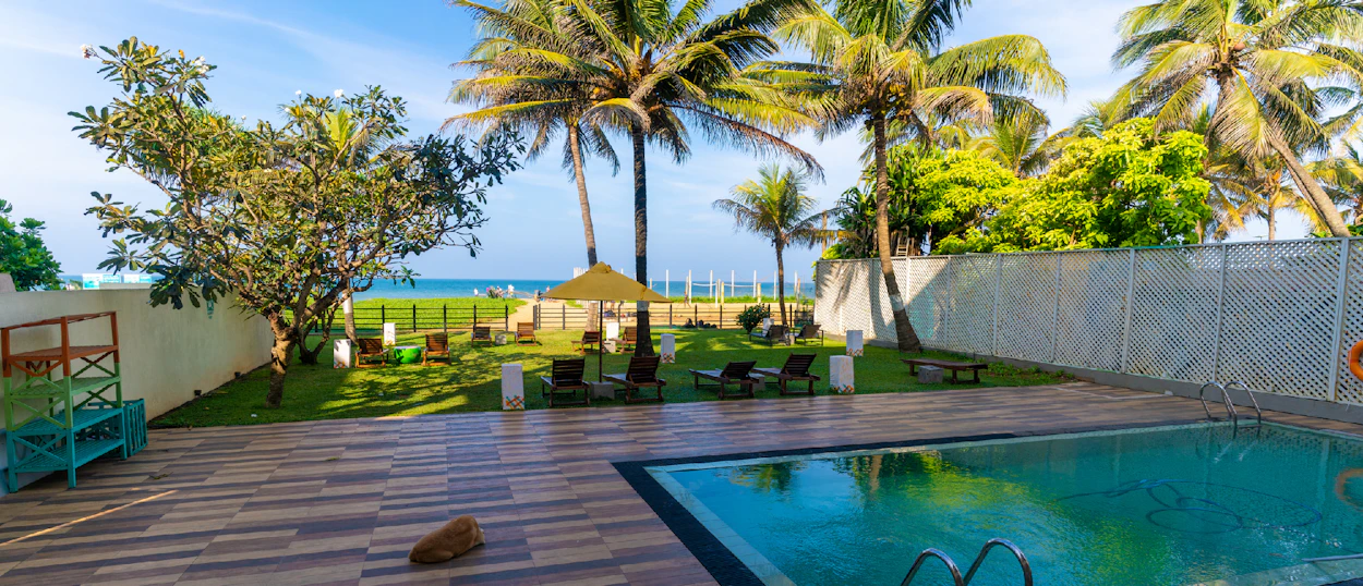 Relaxing hotel garden in Colombo, Sri Lanka, with a pool, palm trees, and ocean view.
