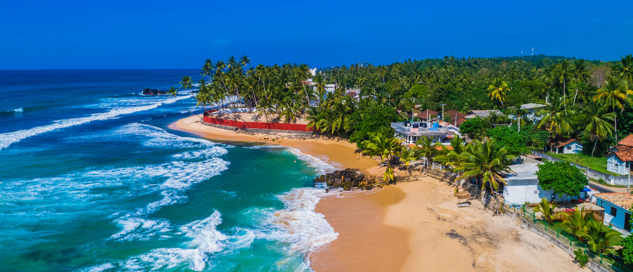 Beautiful tropical beach with turquoise ocean waves, golden sand, and lush palm trees in Sri Lanka.