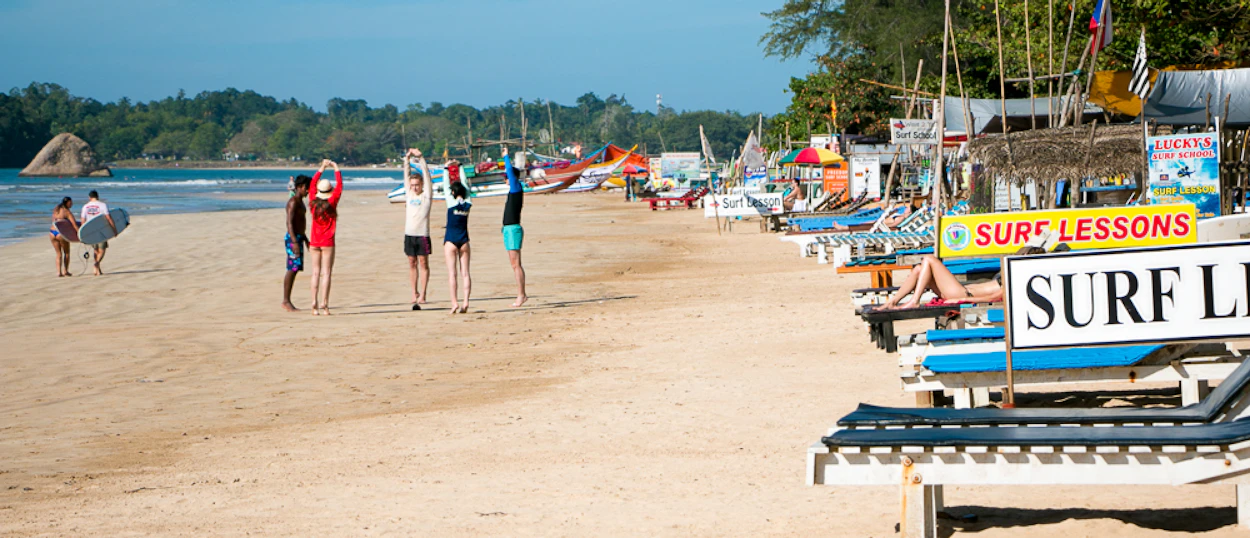 People stretching on Weligama Beach, Sri Lanka, with surf lessons and fishing boats.