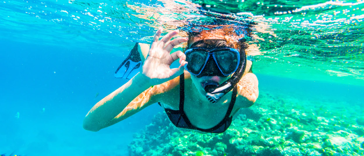 Happy woman snorkeling in clear blue water near Mirissa, Sri Lanka, giving an OK sign.