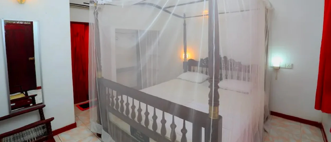 A traditional four-poster bed with a mosquito net in a clean bedroom in Mirissa, Sri Lanka.