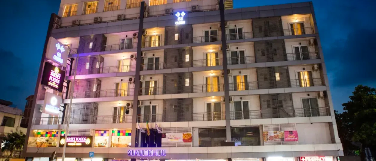 A modern multi-story building with balconies and glowing windows against a dark evening sky.