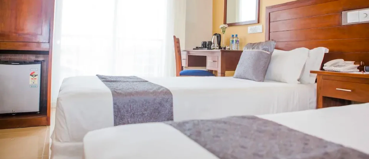 A clean and modern hotel room featuring two beds with white linens and a wooden headboard.