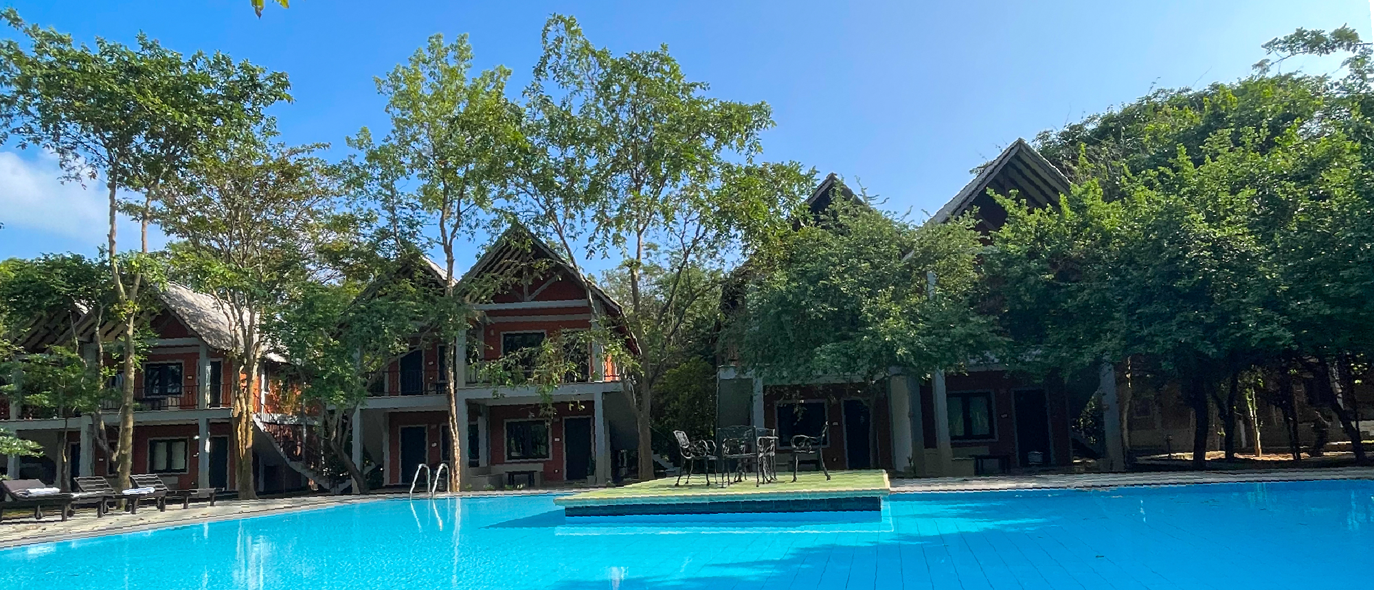 A serene resort pool with charming bungalows and tropical trees under a clear sky in Sigiriya.