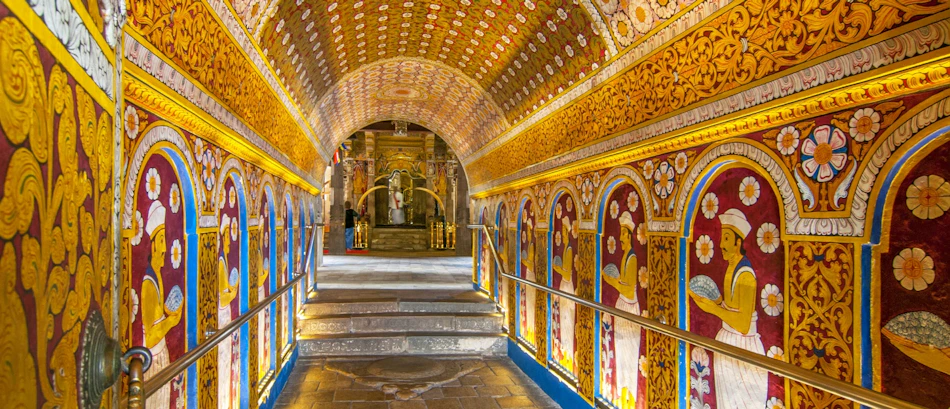 Golden arched hallway with detailed murals and steps inside the sacred Temple of the Tooth, Kandy.