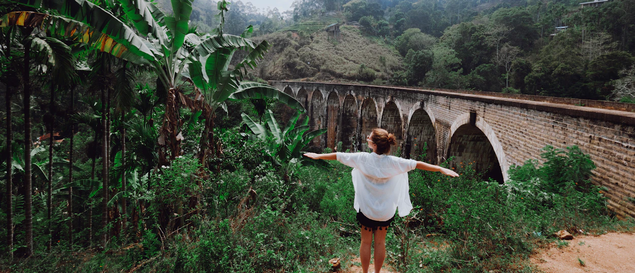 A person with outstretched arms stands before the iconic Nine Arch Bridge in Ella, Sri Lanka.