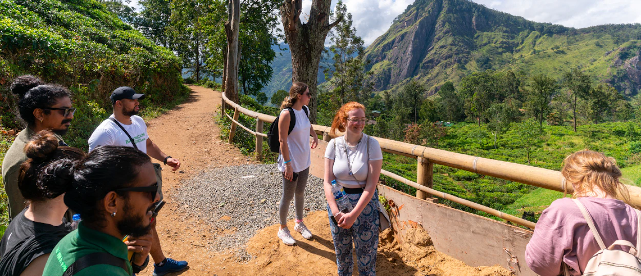 A group of smiling hikers on a trail overlooking lush green mountains in Ella, Sri Lanka.