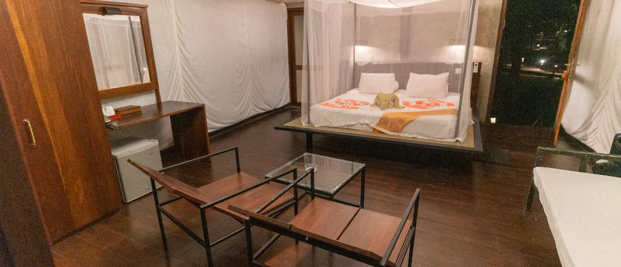A cozy glamping room featuring a large bed with a mosquito net and dark wooden furniture.