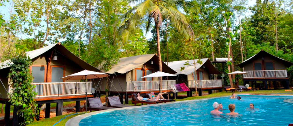 People swim and relax by a pool surrounded by tropical bungalows and palm trees in Weligama.