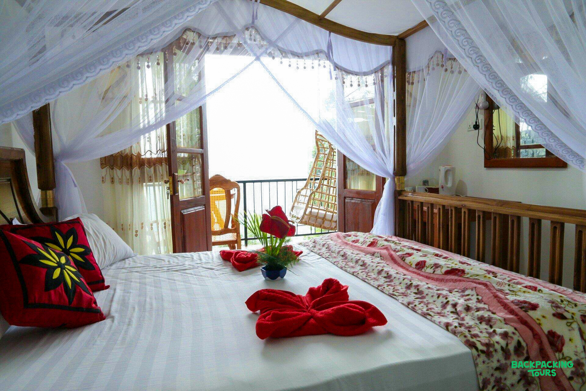 A welcoming bedroom with a four-poster bed, red decor, and a balcony view in Ella.