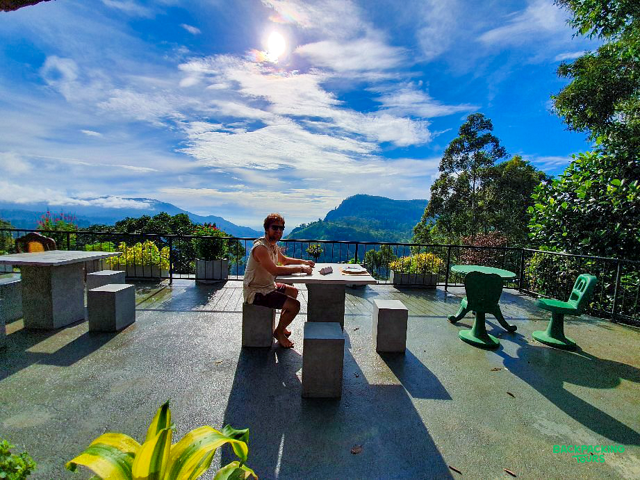 A man dines outdoors with breathtaking views of Sri Lanka's Ella mountains and blue sky.