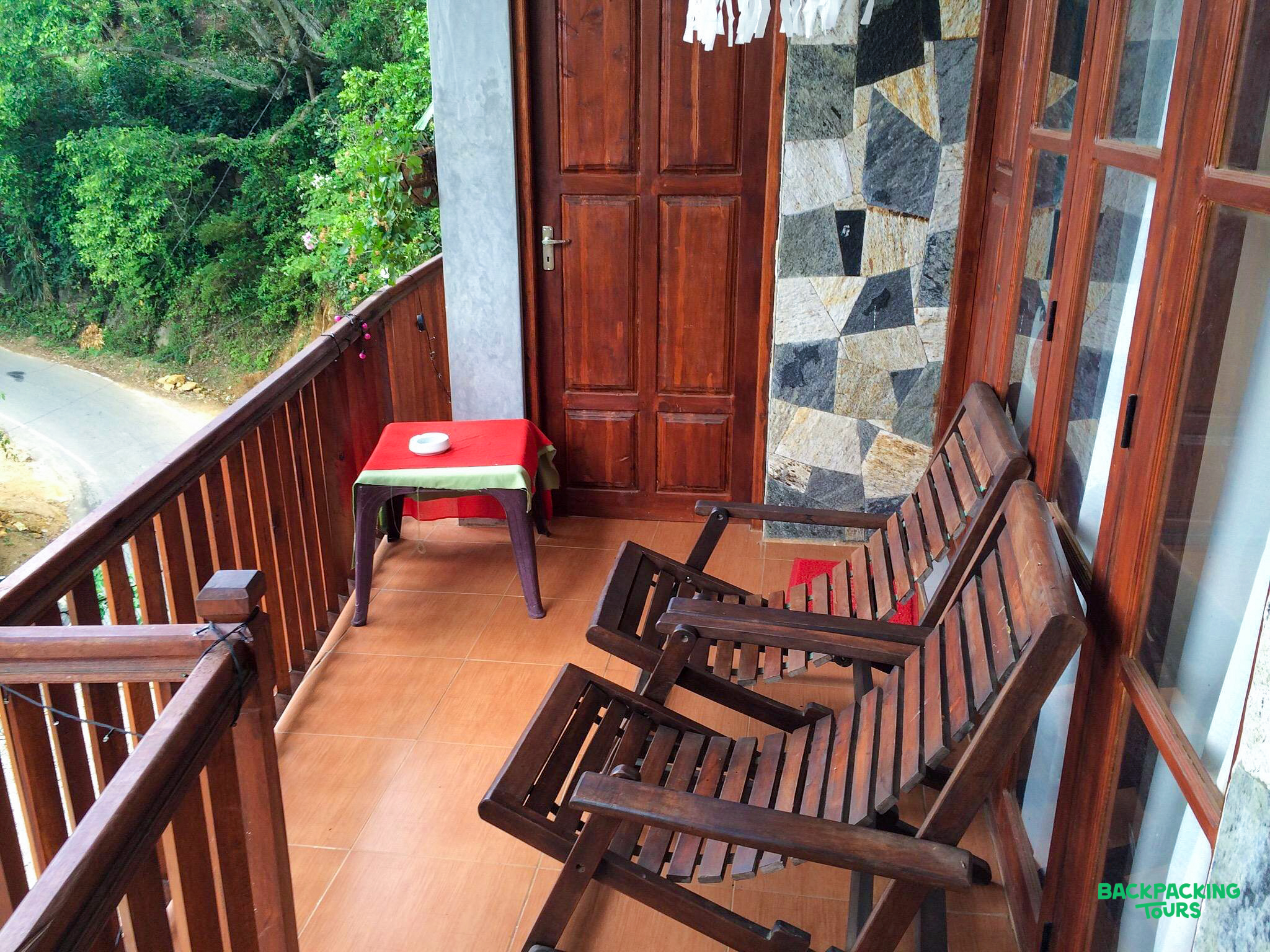 A rustic balcony with wooden chairs and a table, offering a view of the Ella landscape.