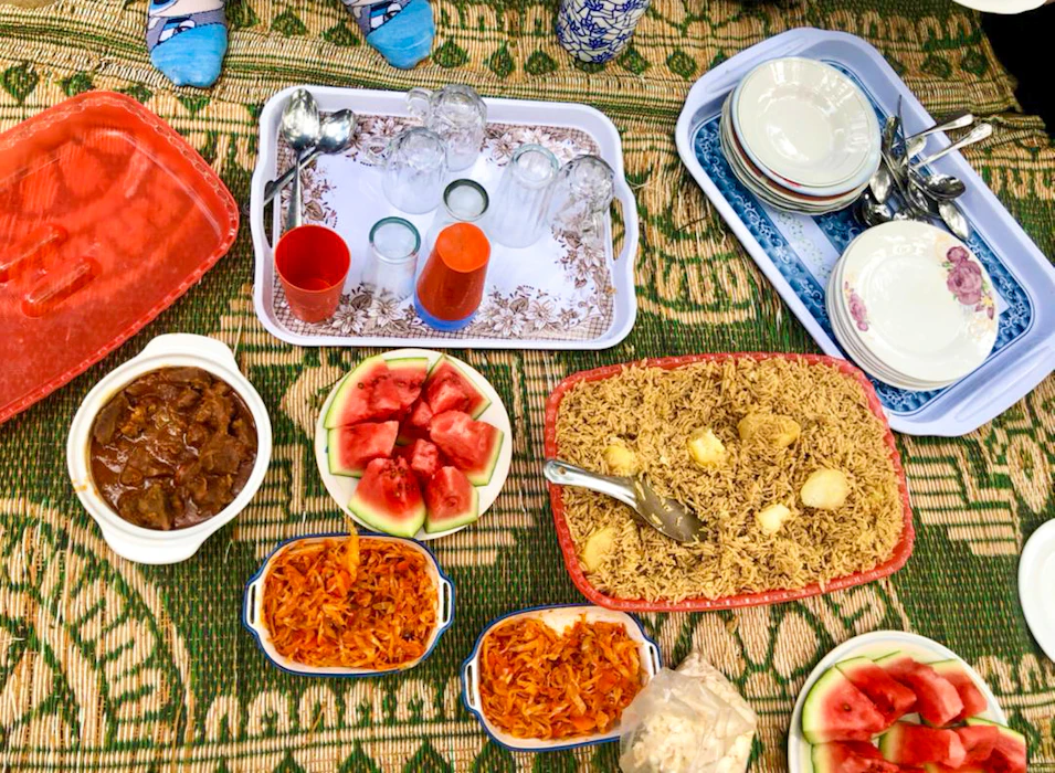 Vibrant communal lunch with rice, stew, and fresh watermelon served on a green mat in Zanzibar.