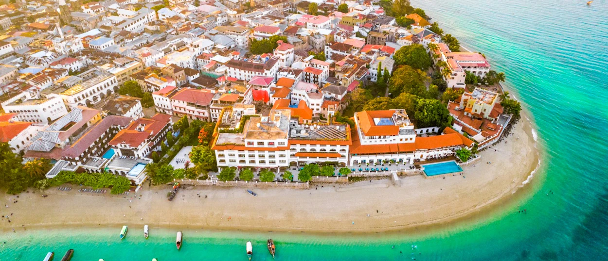Aerial view of Zanzibar's historic town, with buildings, a sandy beach, and turquoise ocean.