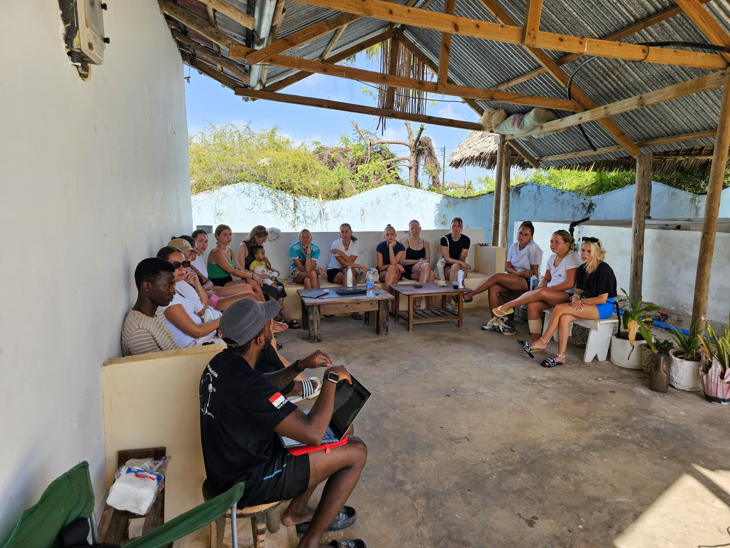 The group sits around the shaded courtyard of the volunteer house for a briefing.