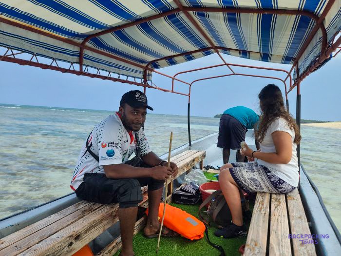 A boatman and volunteers sit under the canopy of a small boat on a turquoise lagoon.