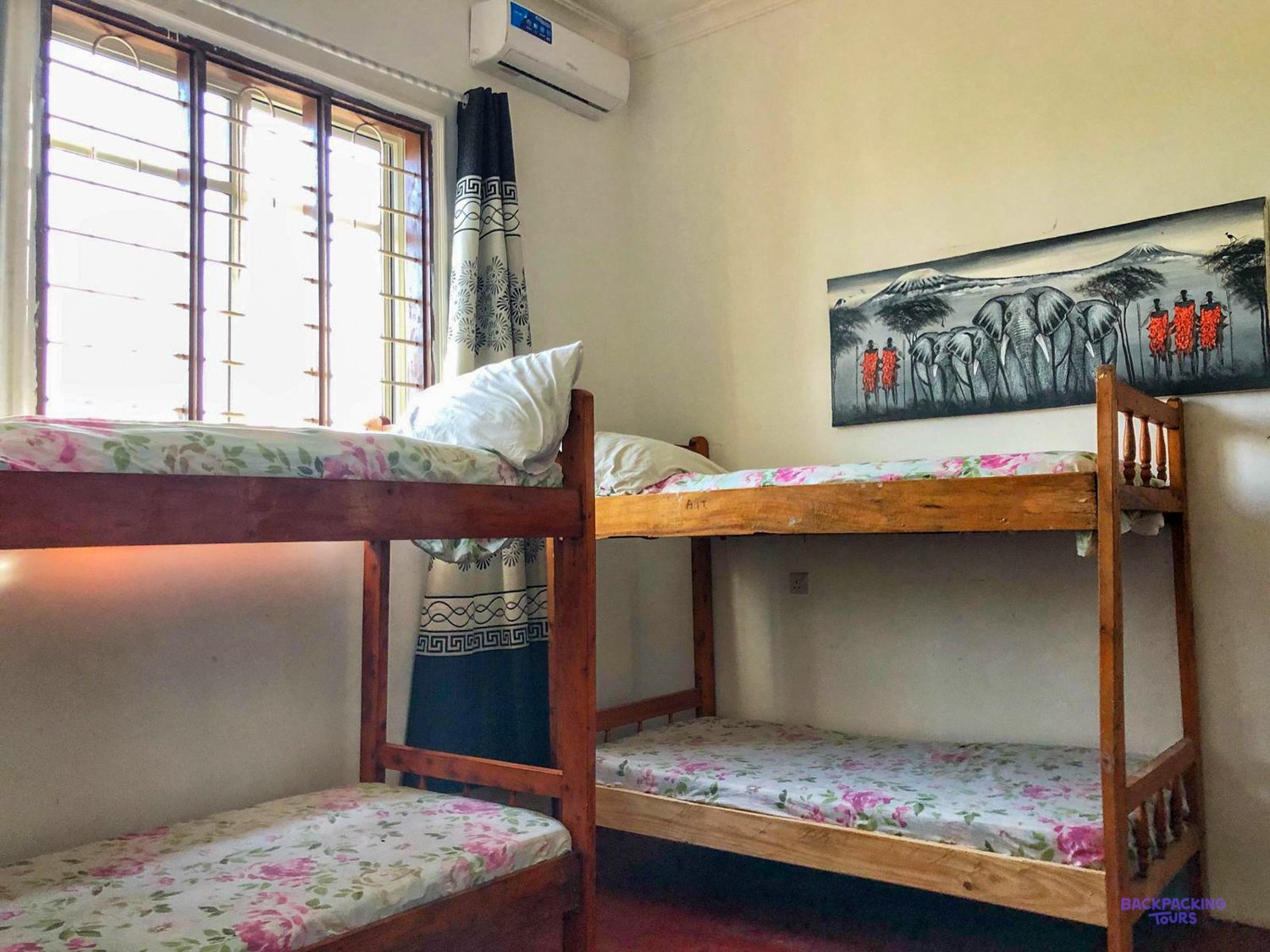 Two wooden bunk beds made up with floral bedding stand beside a bright barred window.