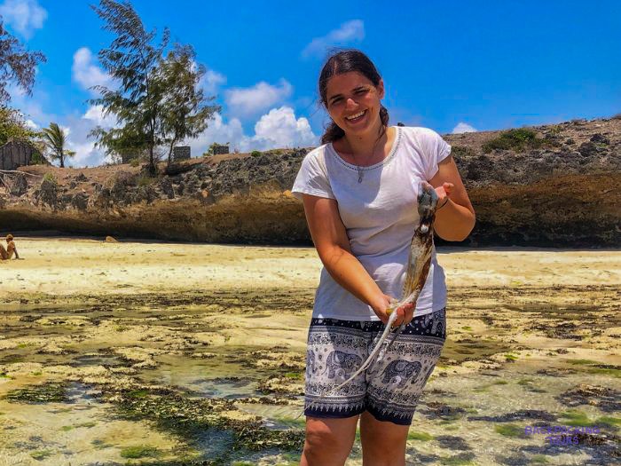 A volunteer stands on the sand holding up something she has found along the shoreline.