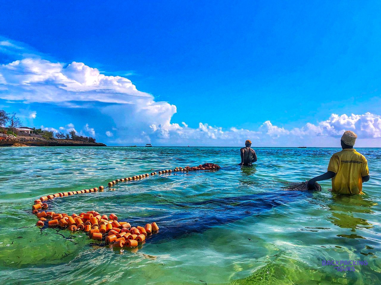 Two men lay a long orange float line across the shallow sea off the reef.