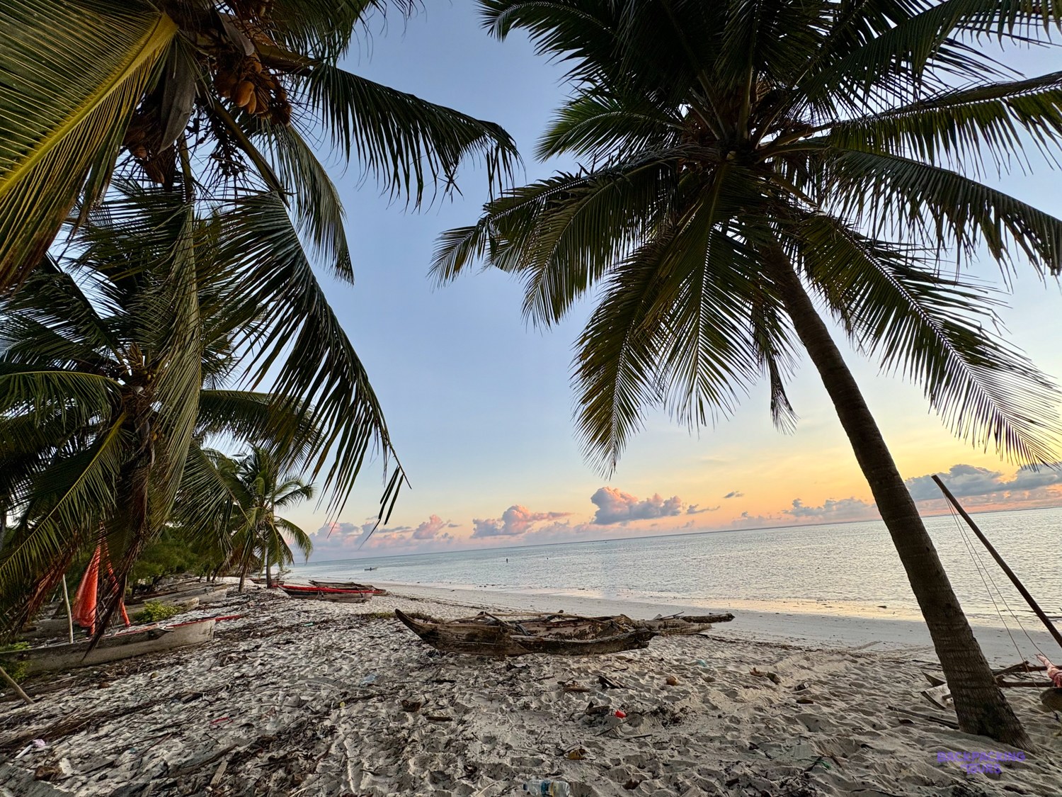 Outrigger canoes rest on the sand under coconut palms as the evening sky turns orange.