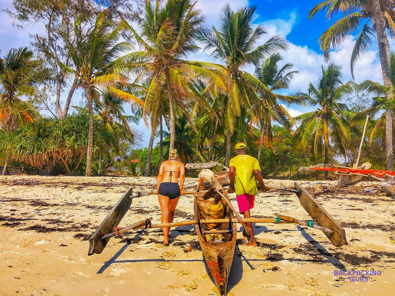 A fisherman and a volunteer move a loaded outrigger canoe down the sand towards the sea.