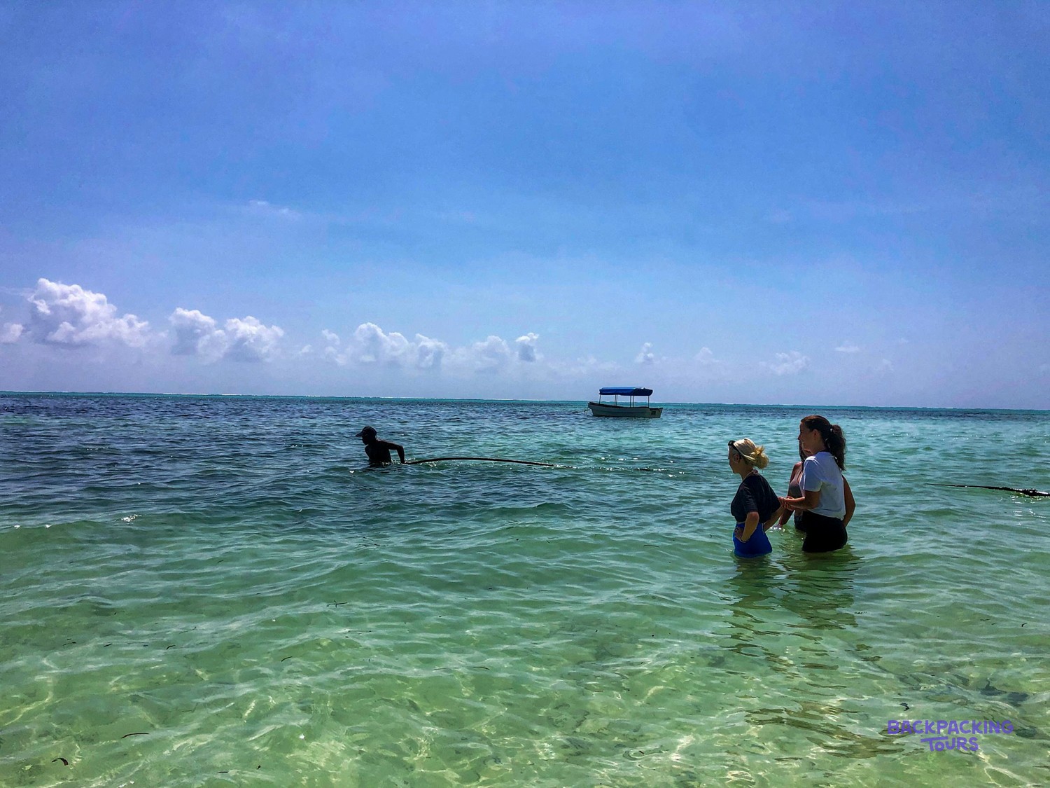 Volunteers stand chest deep in clear water beside a moored boat off the Makunduchi shore.